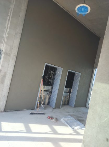 Active stucco work on commercial storefront with gray stucco section and scaffolding